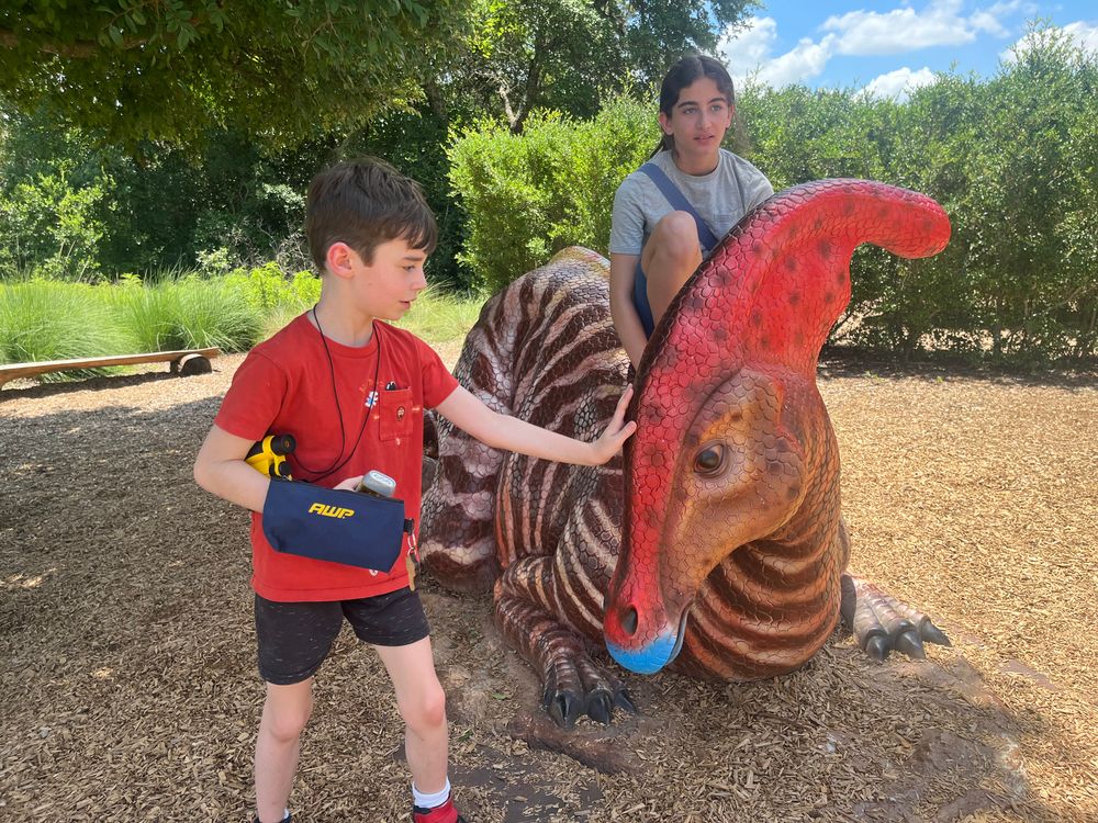 A boy with his hand on the head of a large hadrosaur