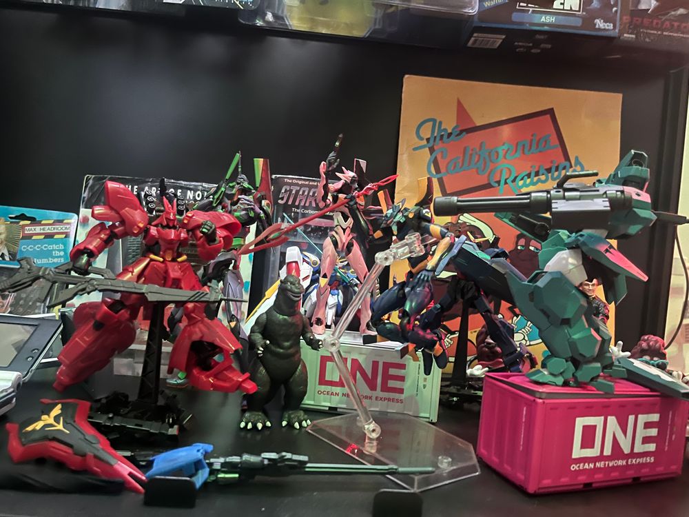 A cluster of brightly colored plastic robots pointing weapons at each other. Godzilla is in the middle, looking confused.