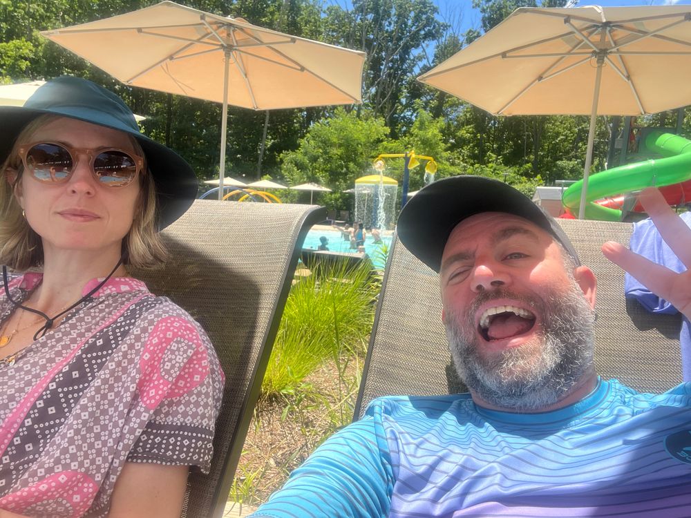 2 people sitting on deck chairs next to a pool