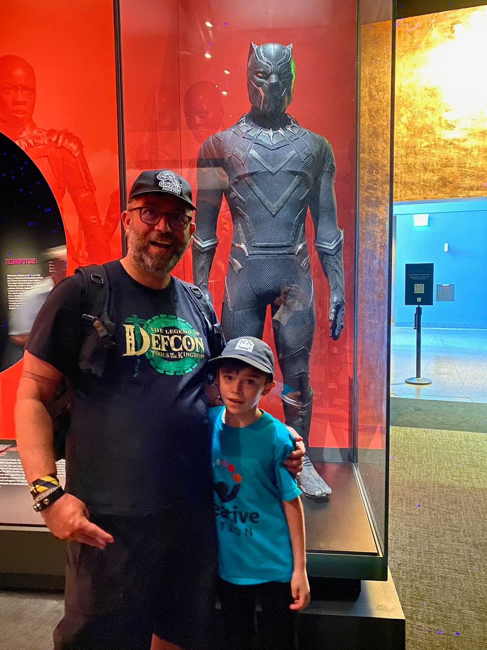 A man and his son standing in front of the Black Panther costume 