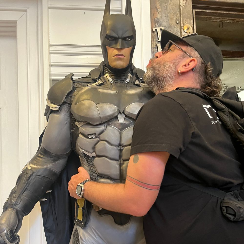 A goofy looking man hugging and attempting to kiss a life-sized Batman statue