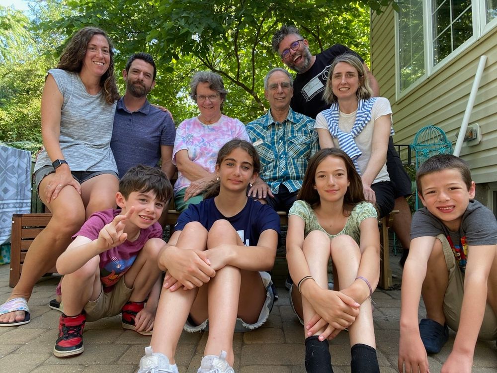 A group of 10 people representing 3 generations of a family, all sitting close together and smiling