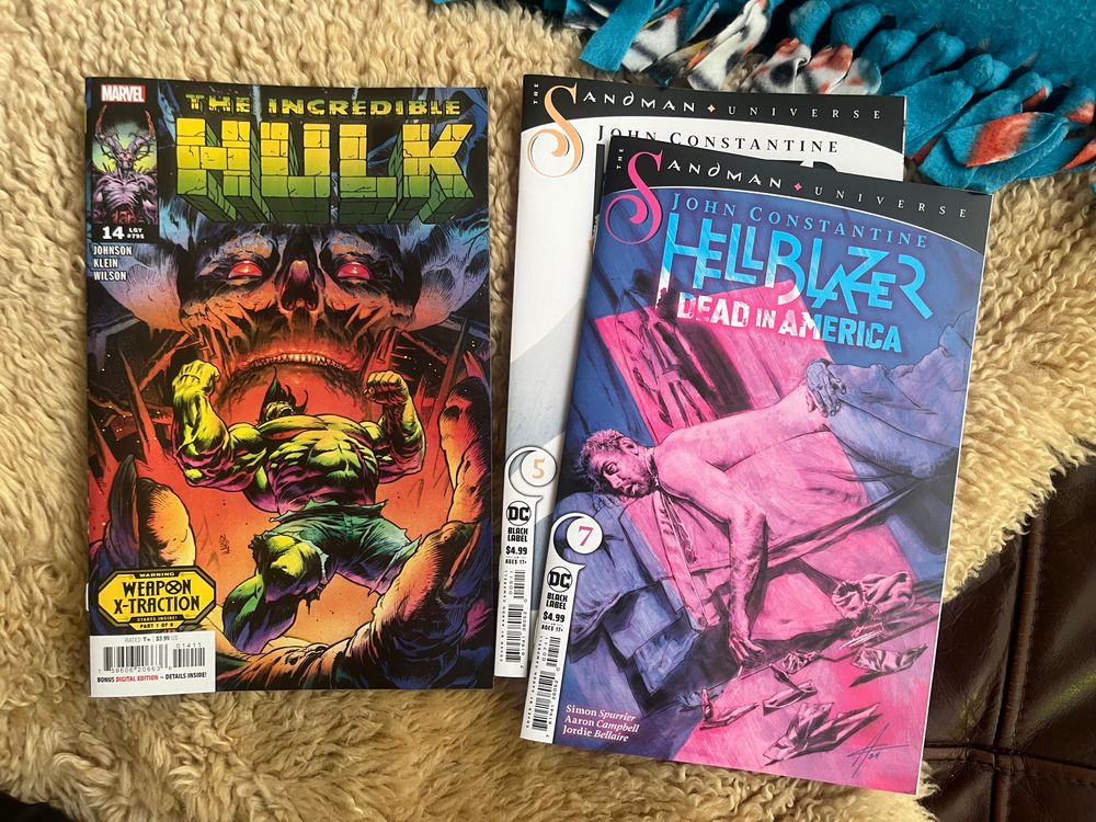 A Hulk comic and a few Hellblazer comics sitting on a fur rug