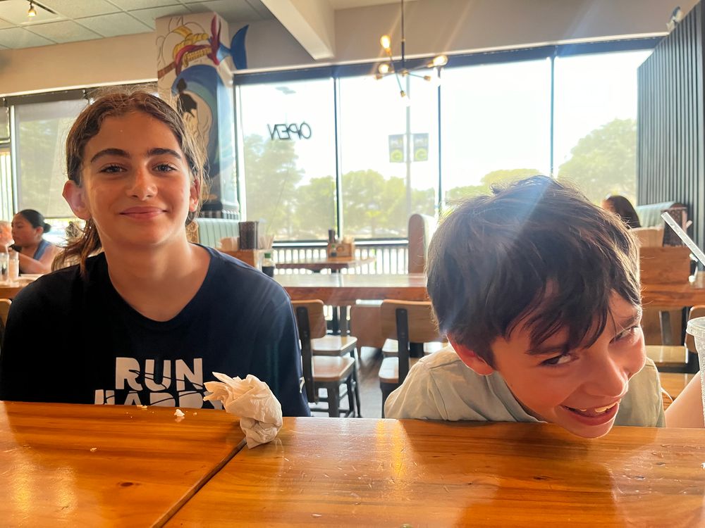 Two kids sitting at a wooden table with big smiles on their faces